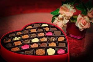 Heart-shaped box of chocolates next to roses.